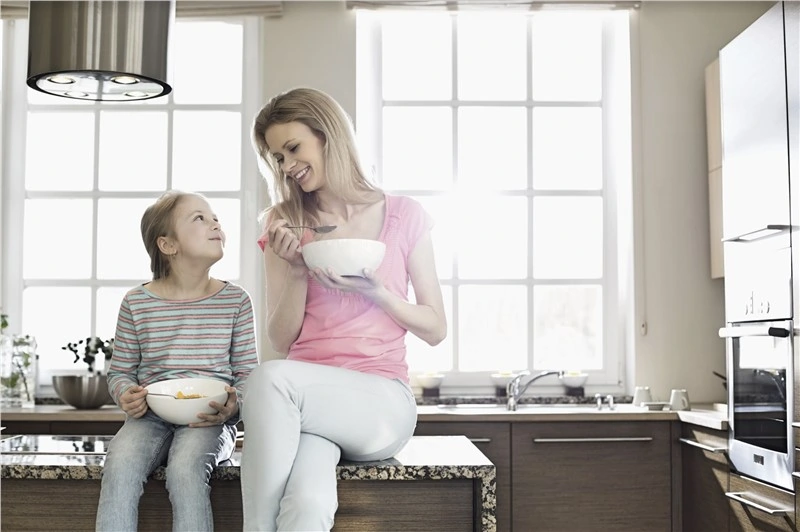 A mother and daughter enjoying a bowl of cereal together in a cozy kitchen.