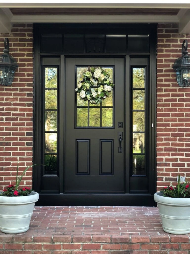 A black front door adorned with a wreath and potted plants, creating a welcoming entrance.