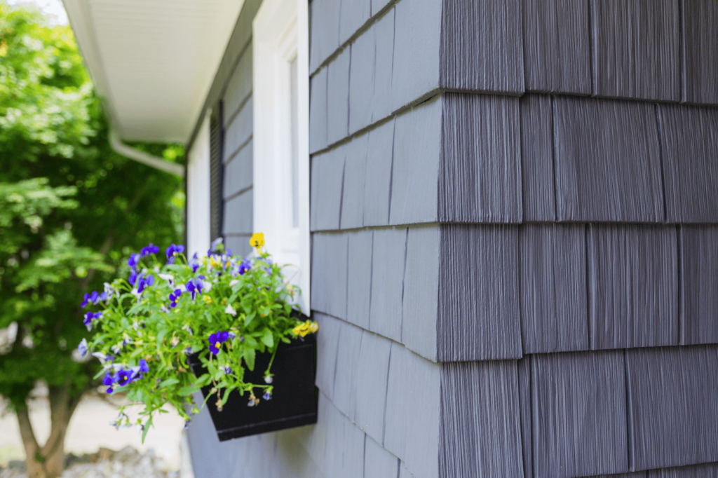 Close-up view of a home's exterior featuring modern gray siding, complemented by a vibrant window flower box, illustrating the impact of choosing home siding on your property's aesthetic appeal.