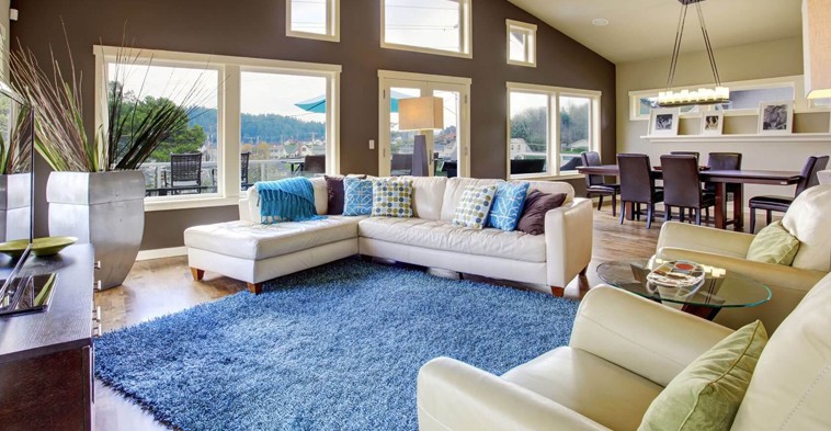 A living room with large windows and a blue rug.