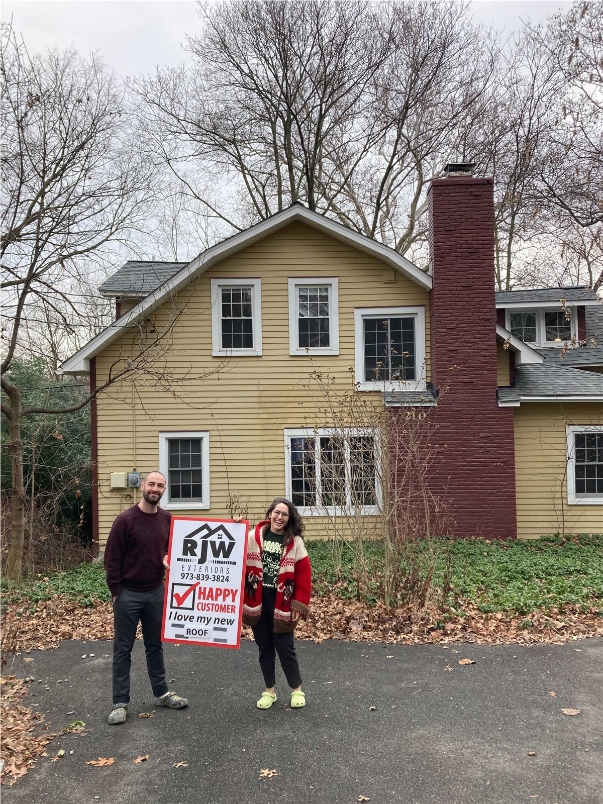 Two people standing in front of a house with a sign.