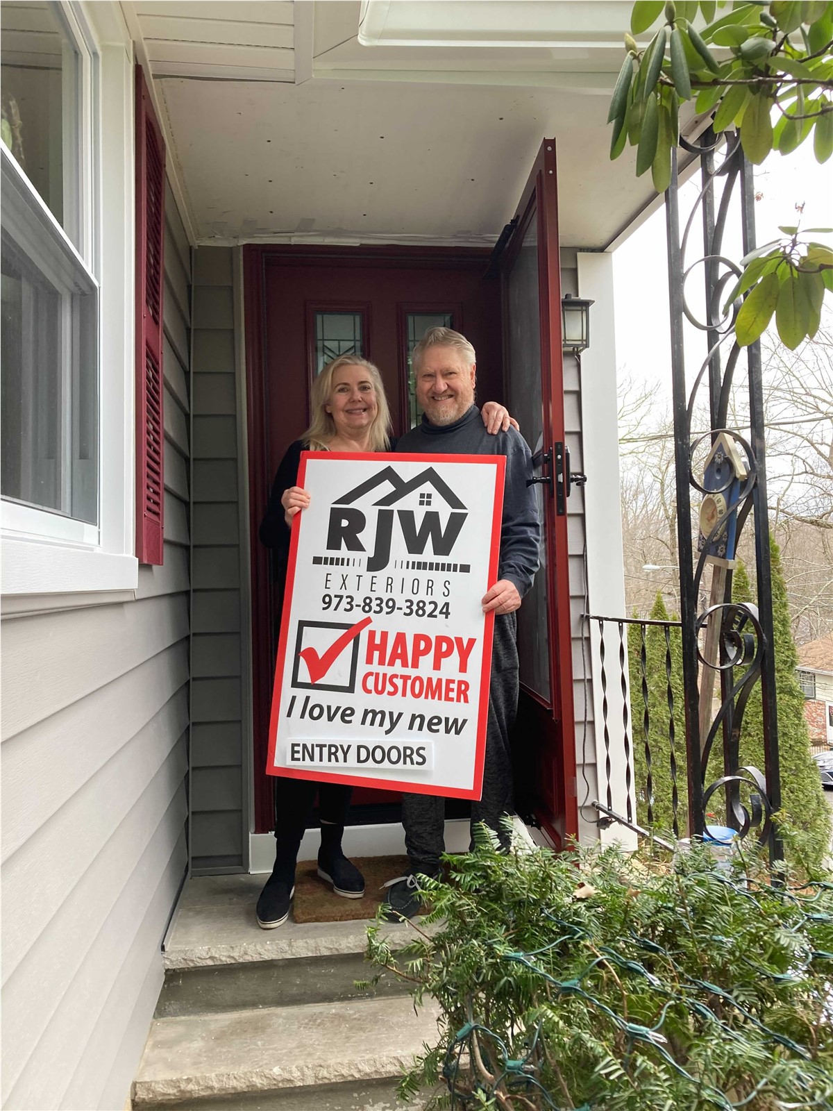 Two people standing on the steps of a house holding a sign that says happy new home.