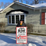 A man standing in front of a house with a sign saying happy happy happy.