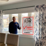 A man standing in front of a window with a sign that says happy home.