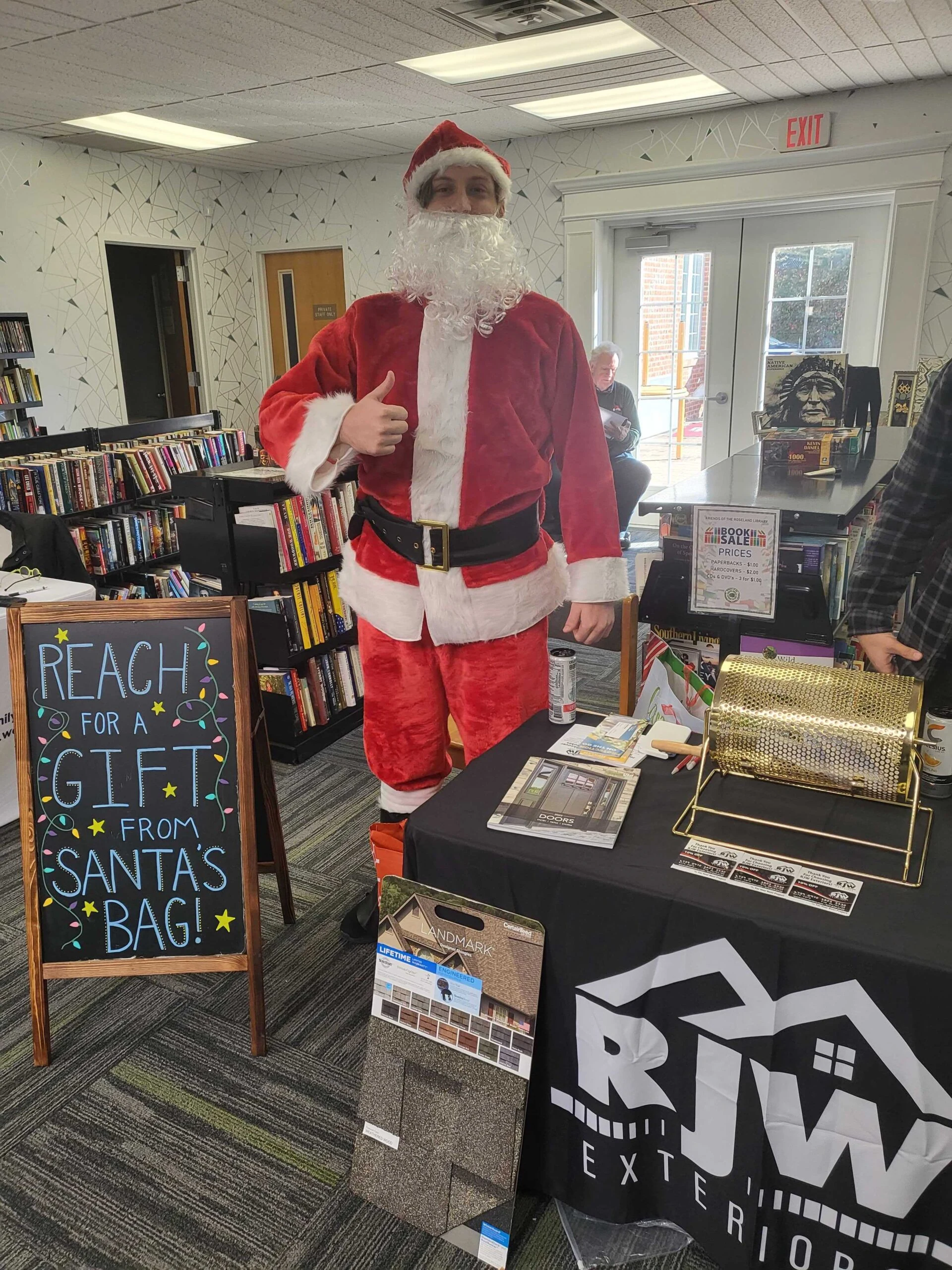 A santa claus is standing next to a table full of books.