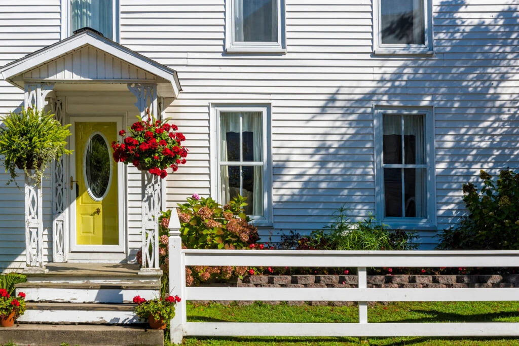Inviting home entrance with a vibrant yellow door and lush hanging flower baskets, exemplifying the 2024 exterior remodeling trend of adding pops of color for enhanced curb appeal.