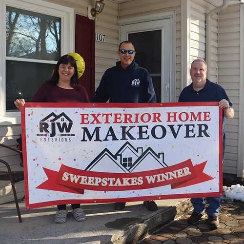 Three individuals posing with a banner celebrating a "exterior home makeover sweepstakes winner.