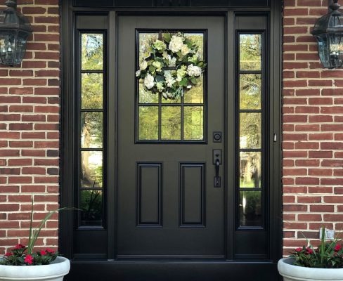 A black front door adorned with a wreath and potted plants, creating a welcoming entrance.