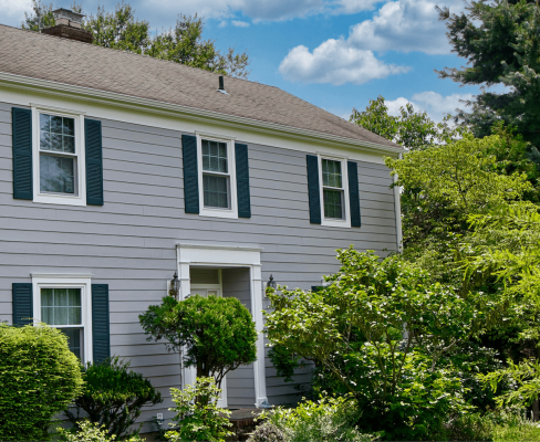 Classic home with gray siding and contrasting green shutters, surrounded by mature landscaping, demonstrating the value of exterior renovation for a high return on investment.