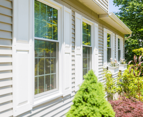 Crisp white replacement windows with shutters on a home's siding, showcasing the longevity and aesthetic value they add to the property, illustrating the lifespan of replacement windows.