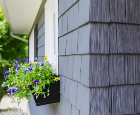 Close-up view of a home's exterior featuring modern gray siding, complemented by a vibrant window flower box, illustrating the impact of choosing home siding on your property's aesthetic appeal.
